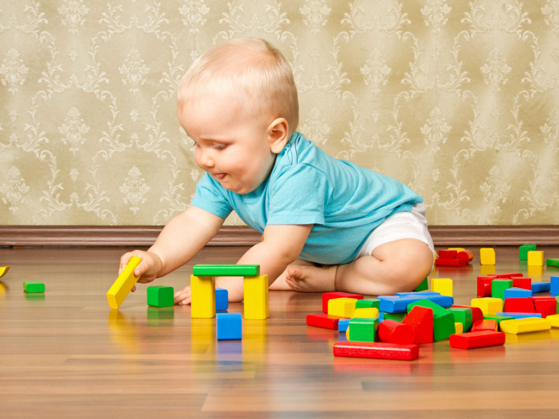 Baby mit blauem T-Shirt spielt mit farbigen Holzklötzen